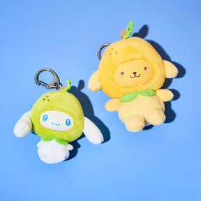 Two plush character keychains on a solid blue background. One is lime green with a white face and white wings, the other is pale yellow with a green collar and a small leaf on its head.