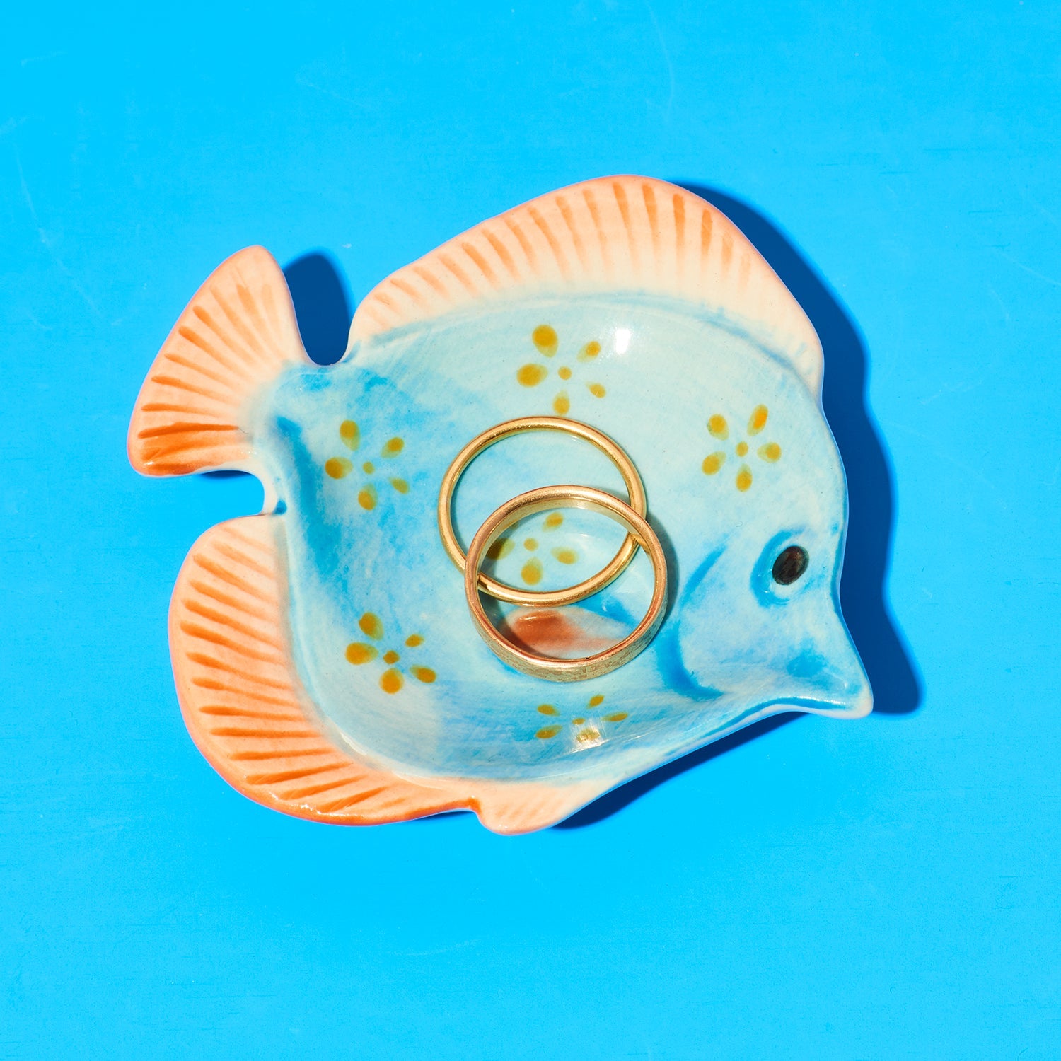 Fish-shaped ring holder with gold rings on a blue background