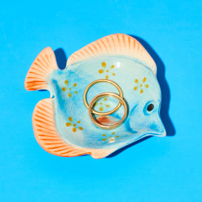 Fish-shaped ring holder with gold rings on a blue background