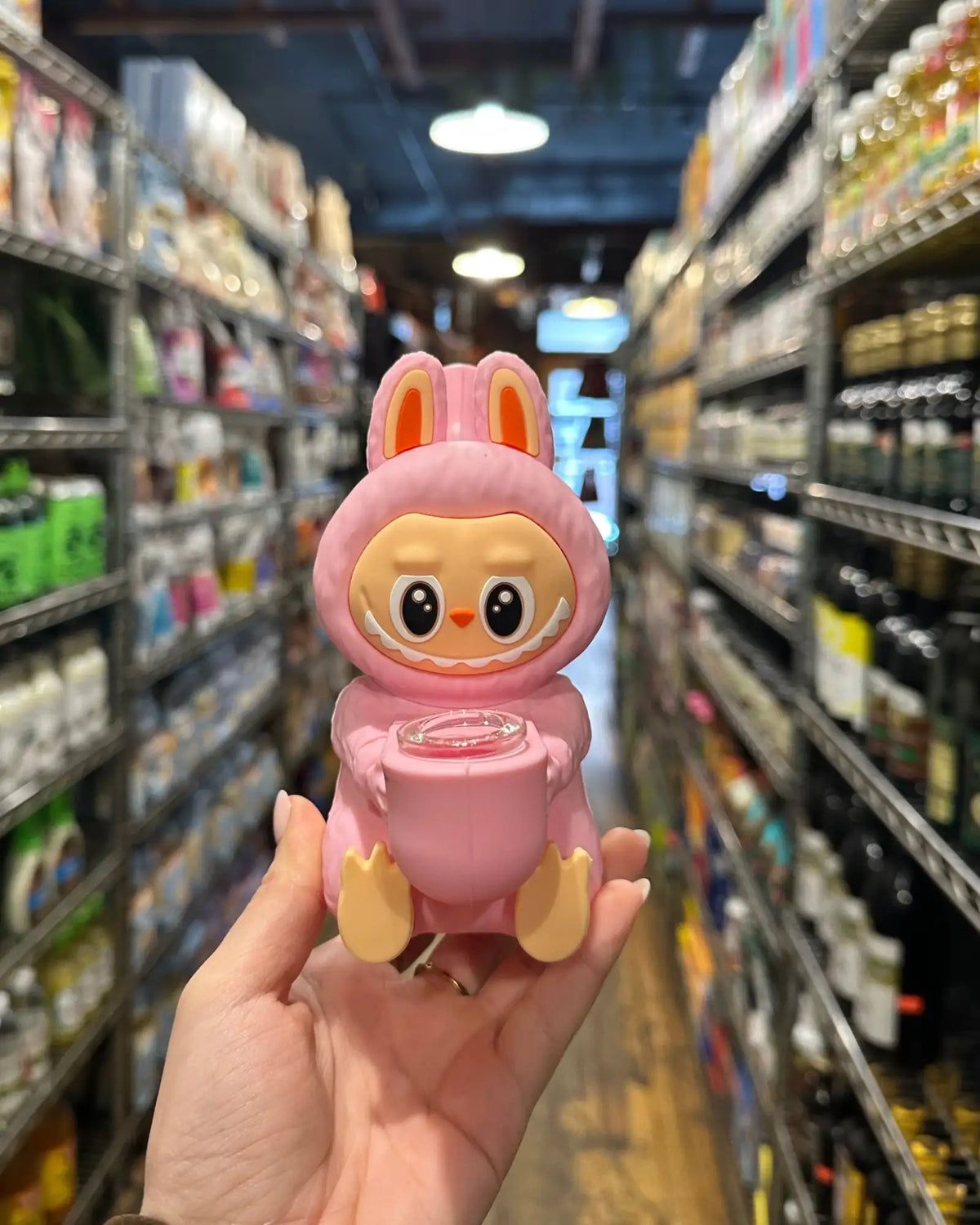 Pink toy labubong figure with bunny ears held in a store aisle