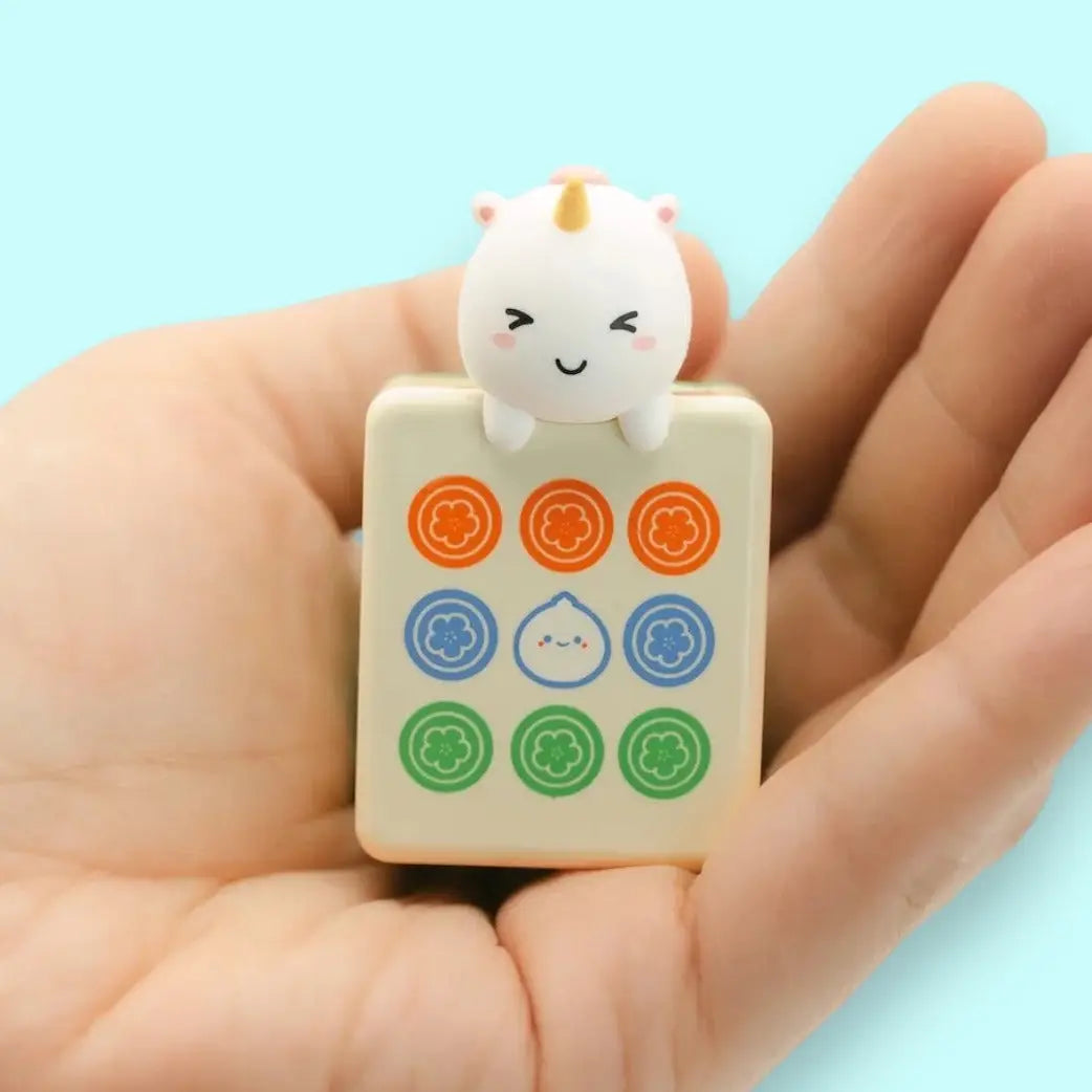 Hand holding a mahjong tile with a cartoon character on a light blue background
