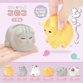 Two cat-shaped squishies, one gray and one yellow, held by hands against a pink background with cat illustrations.