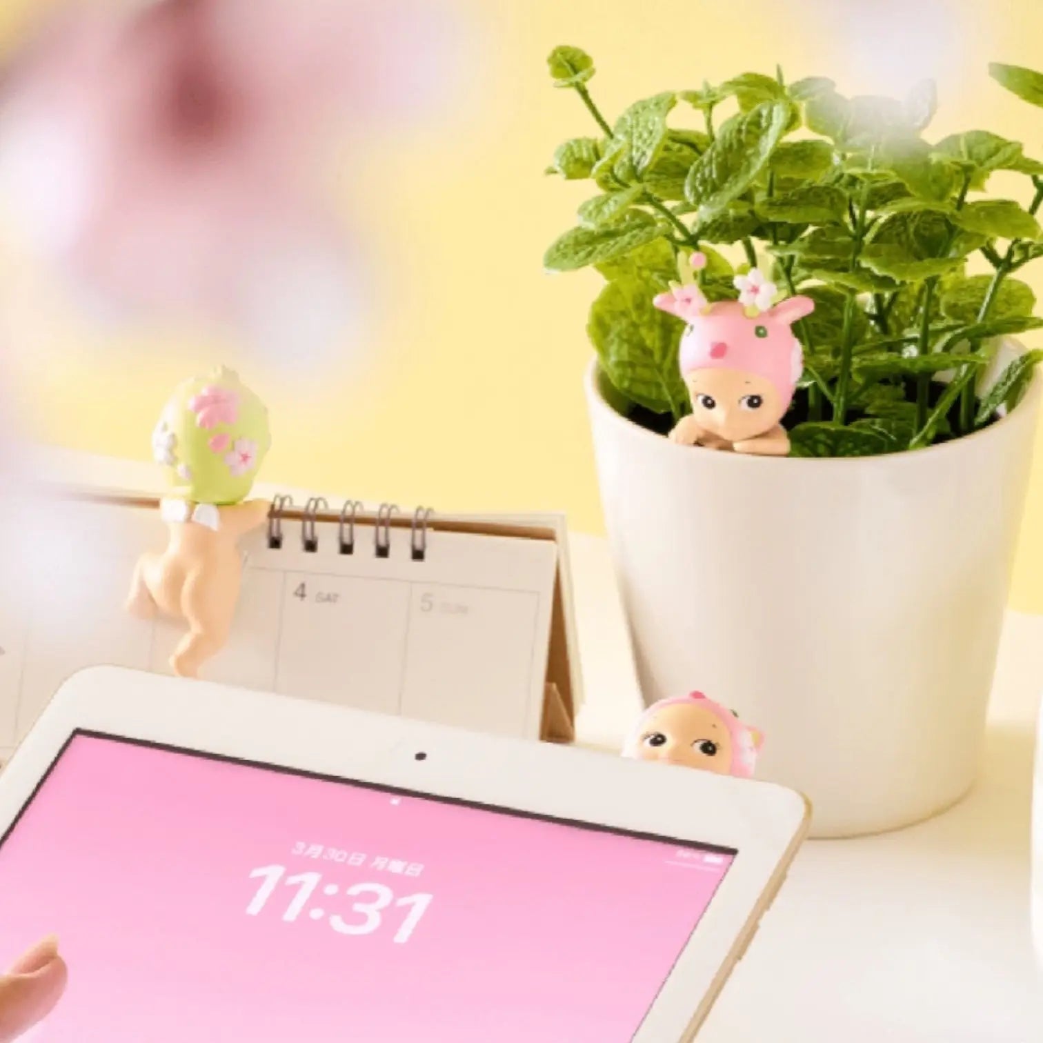 Tablet with pink screen, small plant, and decorative figures on a desk.