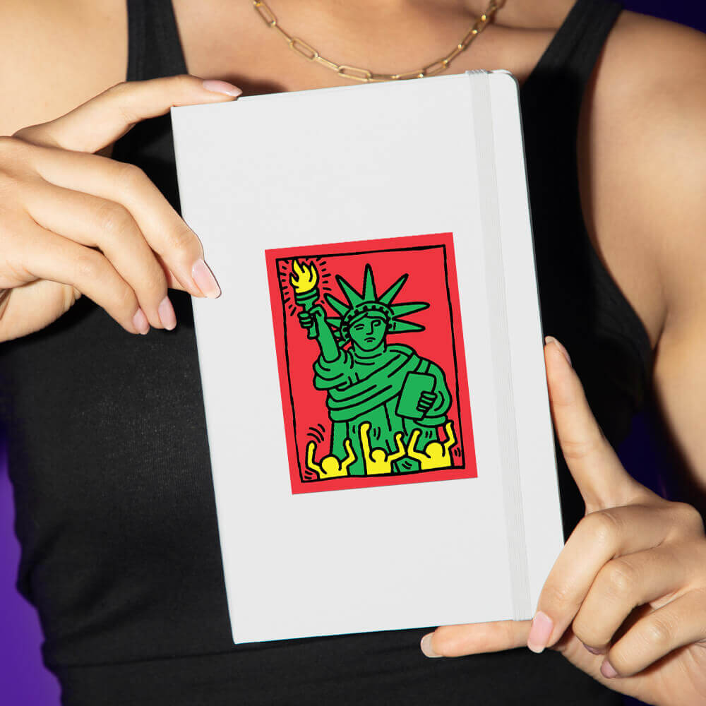 Person holding a white book with a colorful illustration of the Statue of Liberty on a red background.