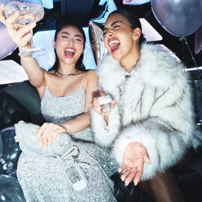 Two women celebrating inside a limousine with balloons and drinks.