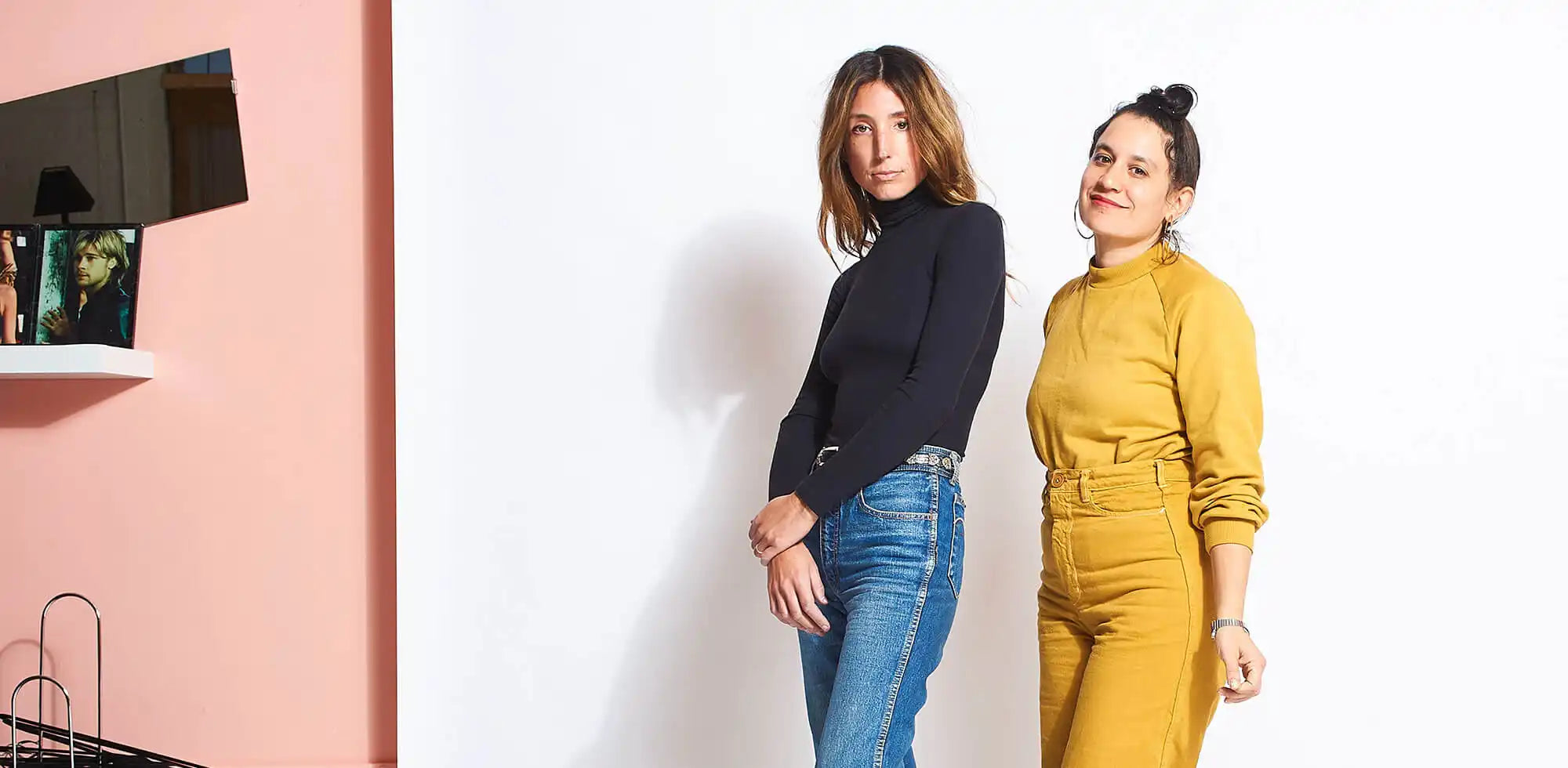 Two people wearing contrasting outfits - one in a black sweater with jeans and another in a mustard yellow jumpsuit.