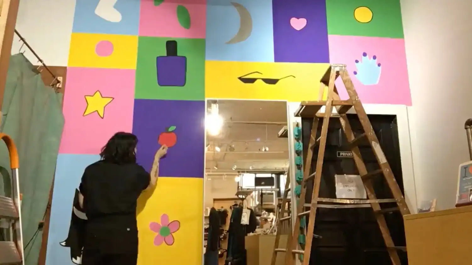 Wooden ladder stands next to a colorful wall mural with various shapes and symbols.